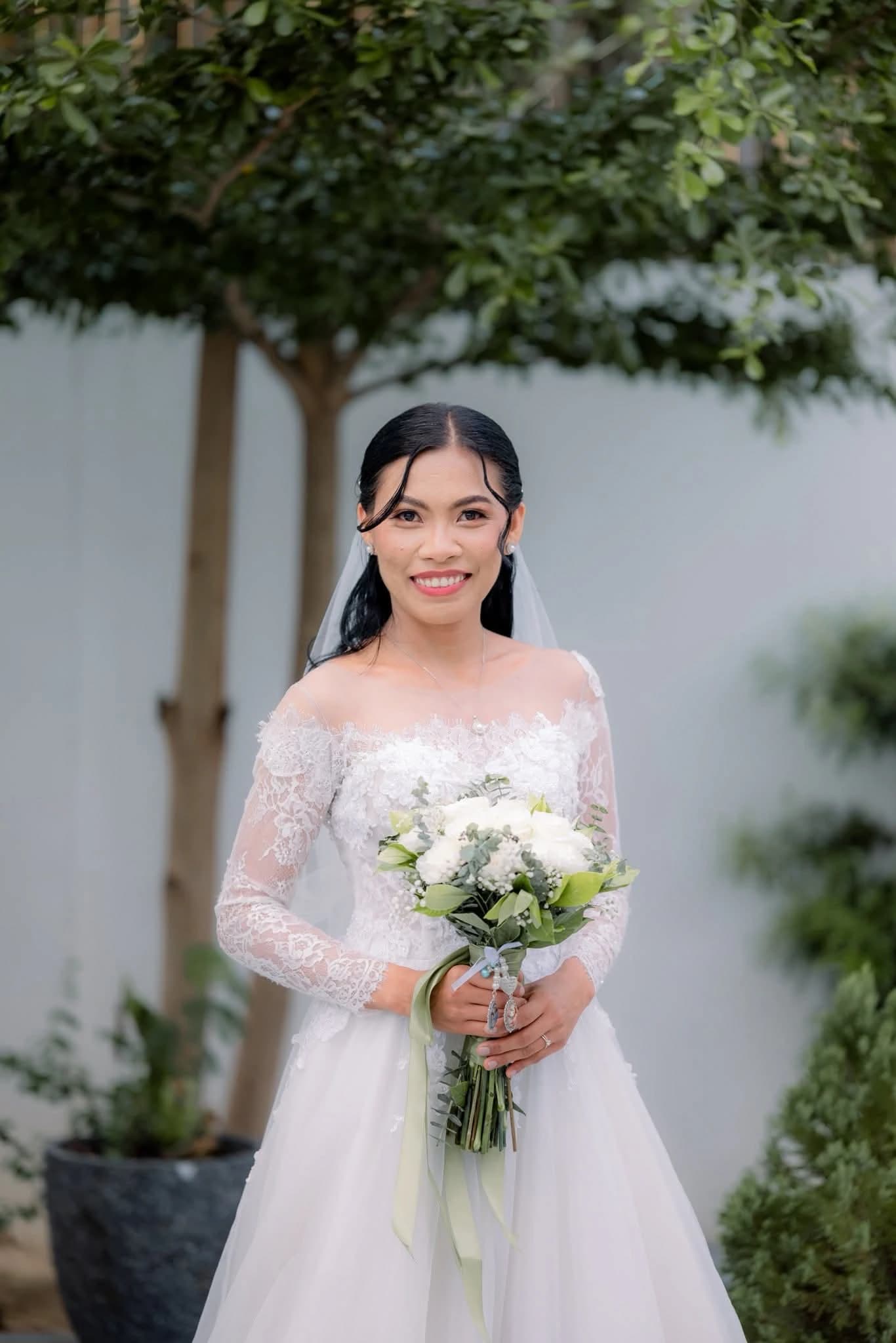 Bride in a pale pink long-sleeved gown holding a white bouquet