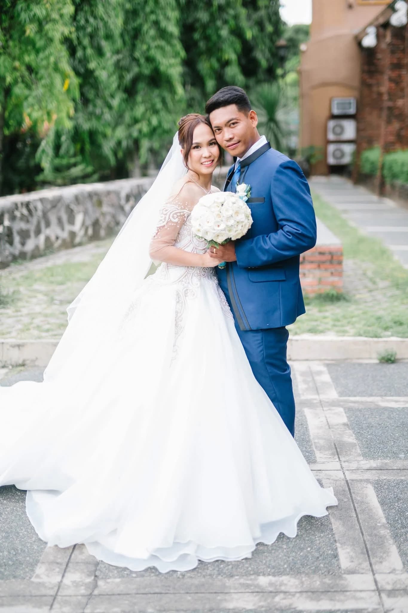 Bride and groom posing outdoors with the groom in a blue suit