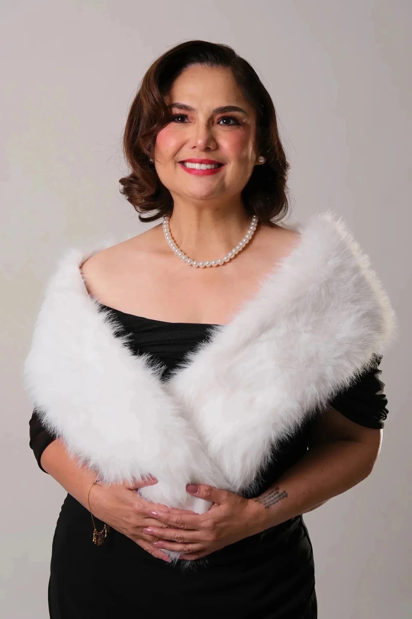 Snooky Serna in a black dress, pearls, and a white stole