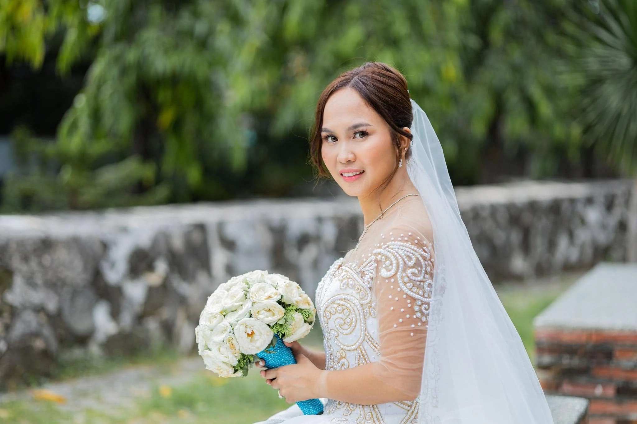 Bridal portrait with luminous wedding makeup, styled hair, and a white bouquet